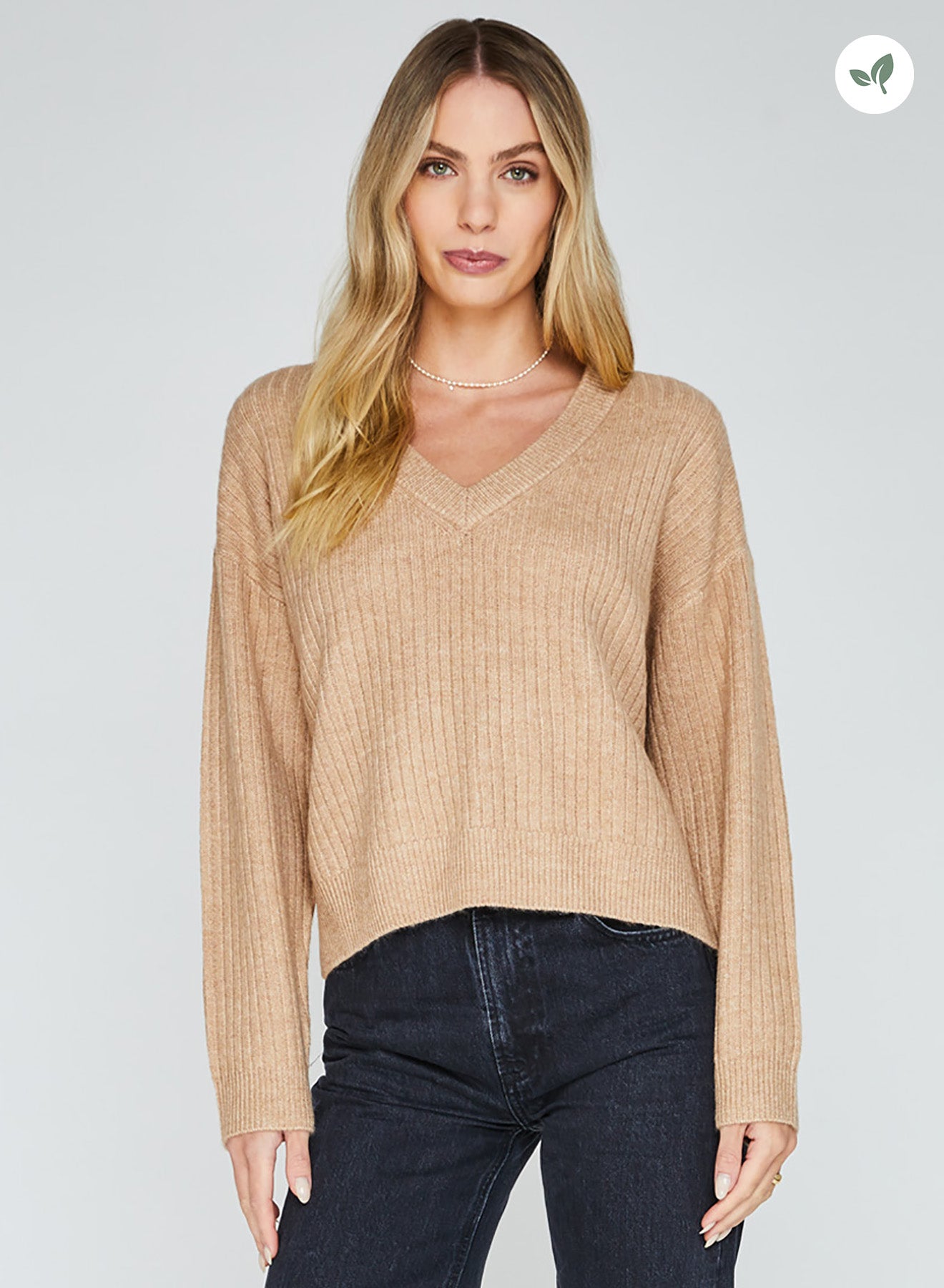 Woman wearing a tan boxy v-neck pullover sweater.