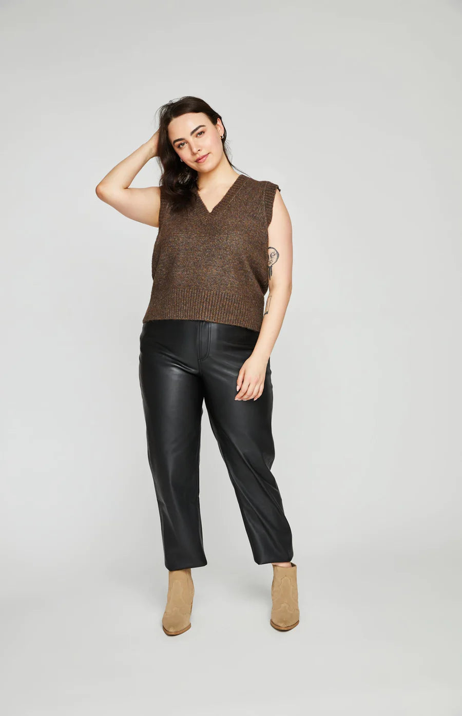 Plus size woman wearing dark brown sweater vest with leather pants.