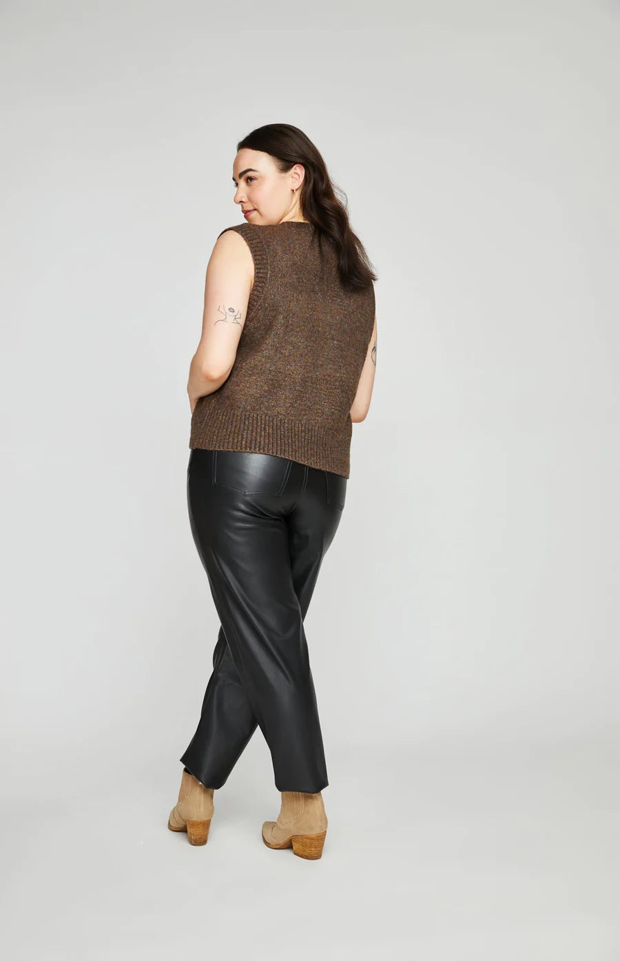 Curvy woman wearing dark brown sweater vest with black leather pant.